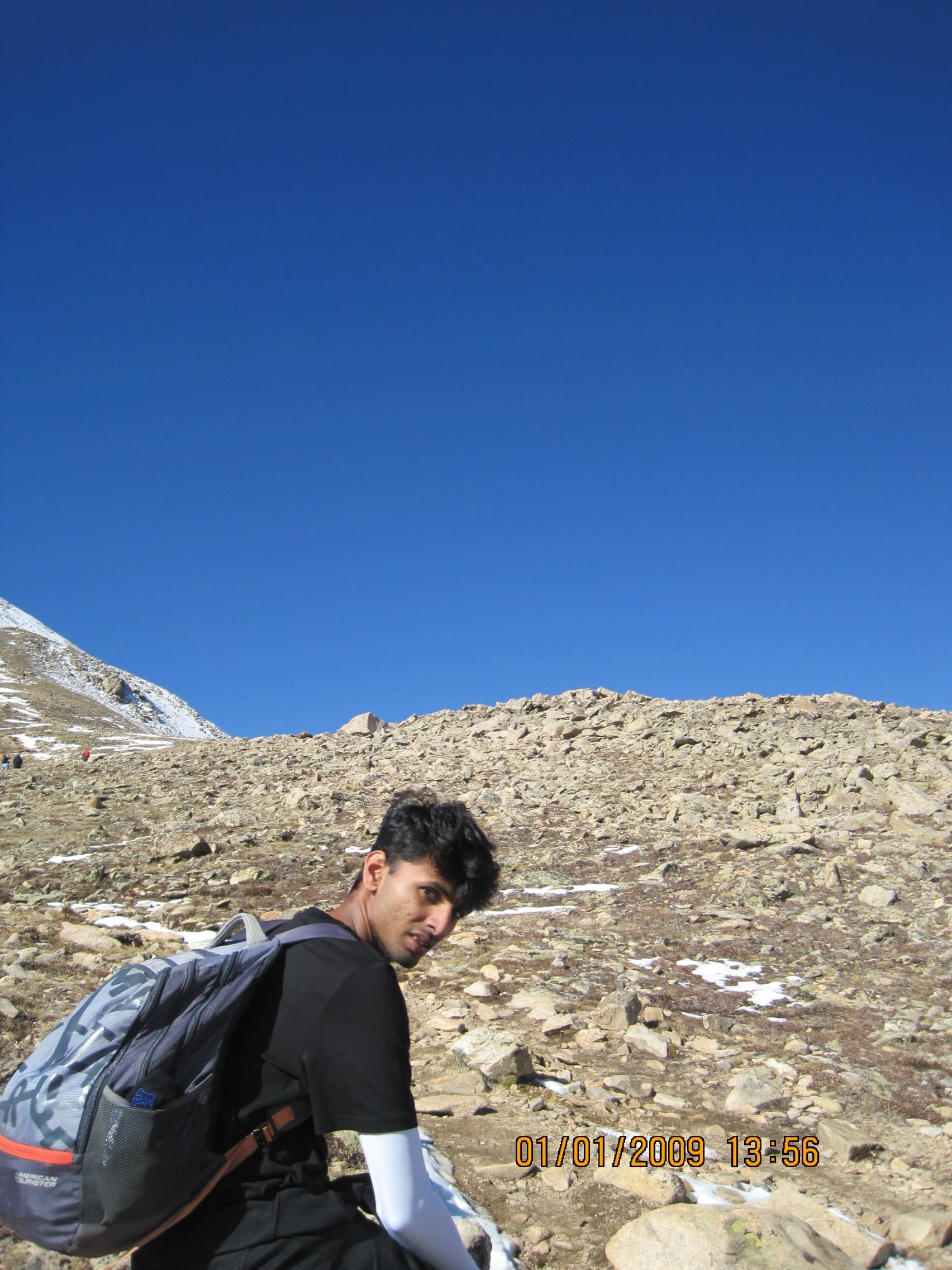 Ansuman with a backpack on a steep rocky slope high on Mount Elbert, looking back at the camera under a deep blue sky